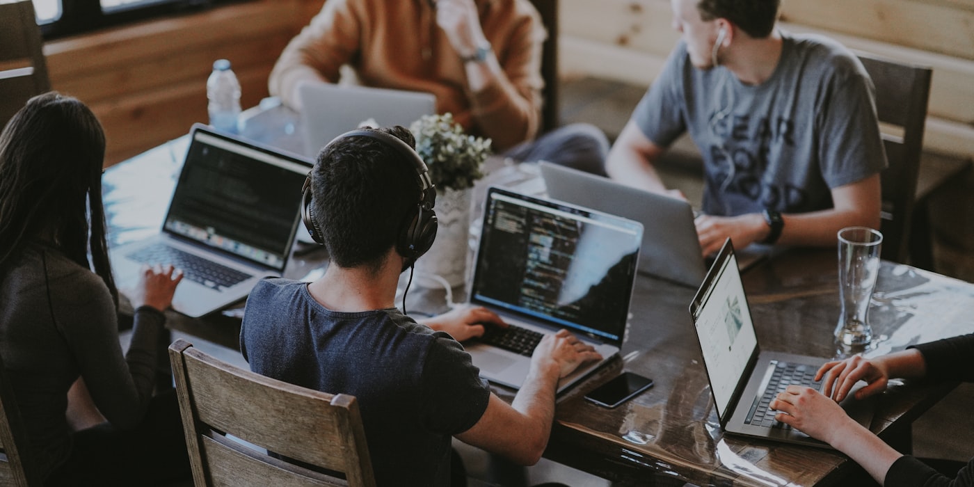 A team working across laptops around a shared table, code open on screen